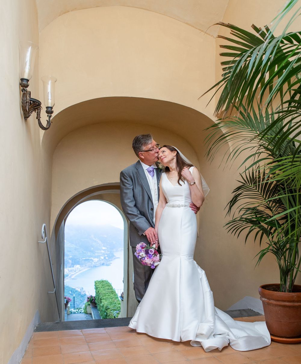 Bride and groom cuddle with scene of Amalfi coast through historic archway
