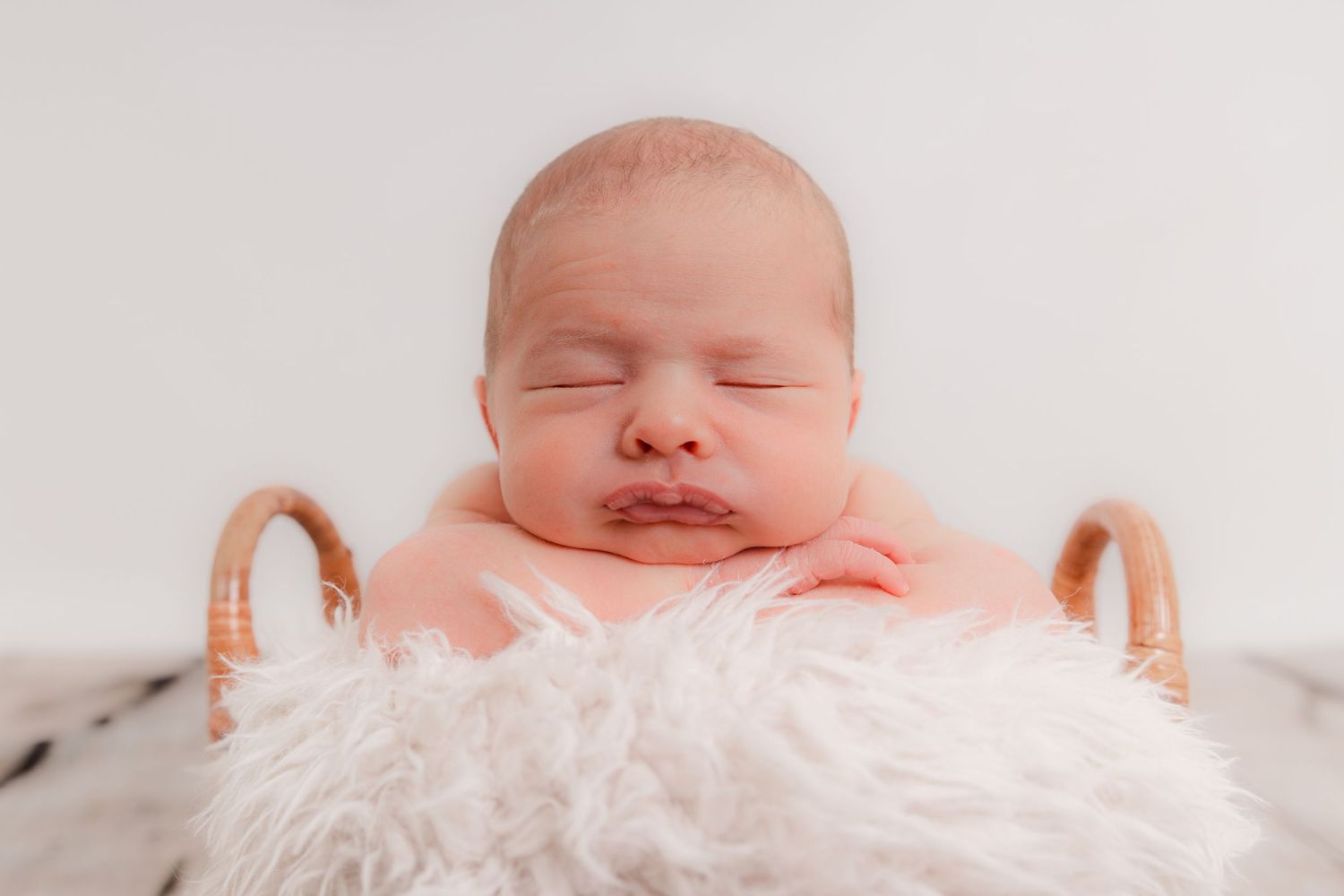 Sleeping newborn baby wearing a headband in a wicker basket with white fur lining. Photographer. Hull. East Yorkshire.
