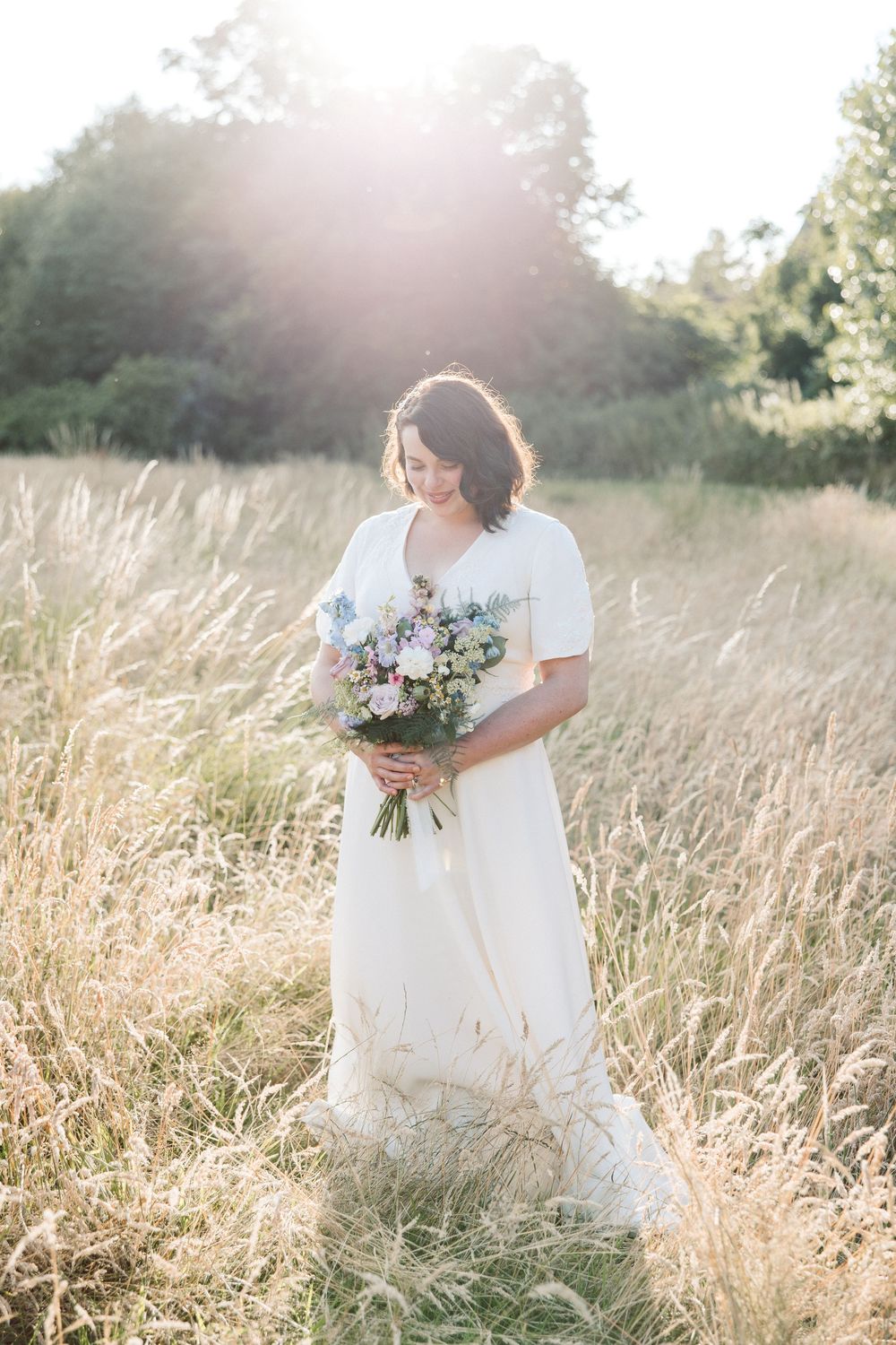Ethereal bridal portraits in a sun-drenched meadow with tall golden grass and a delicate floral bouquet.