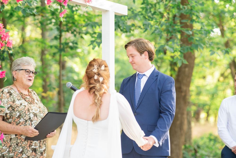 Bride and groom holding hands at outdoor wedding altar decorated with pink floral arrangements.