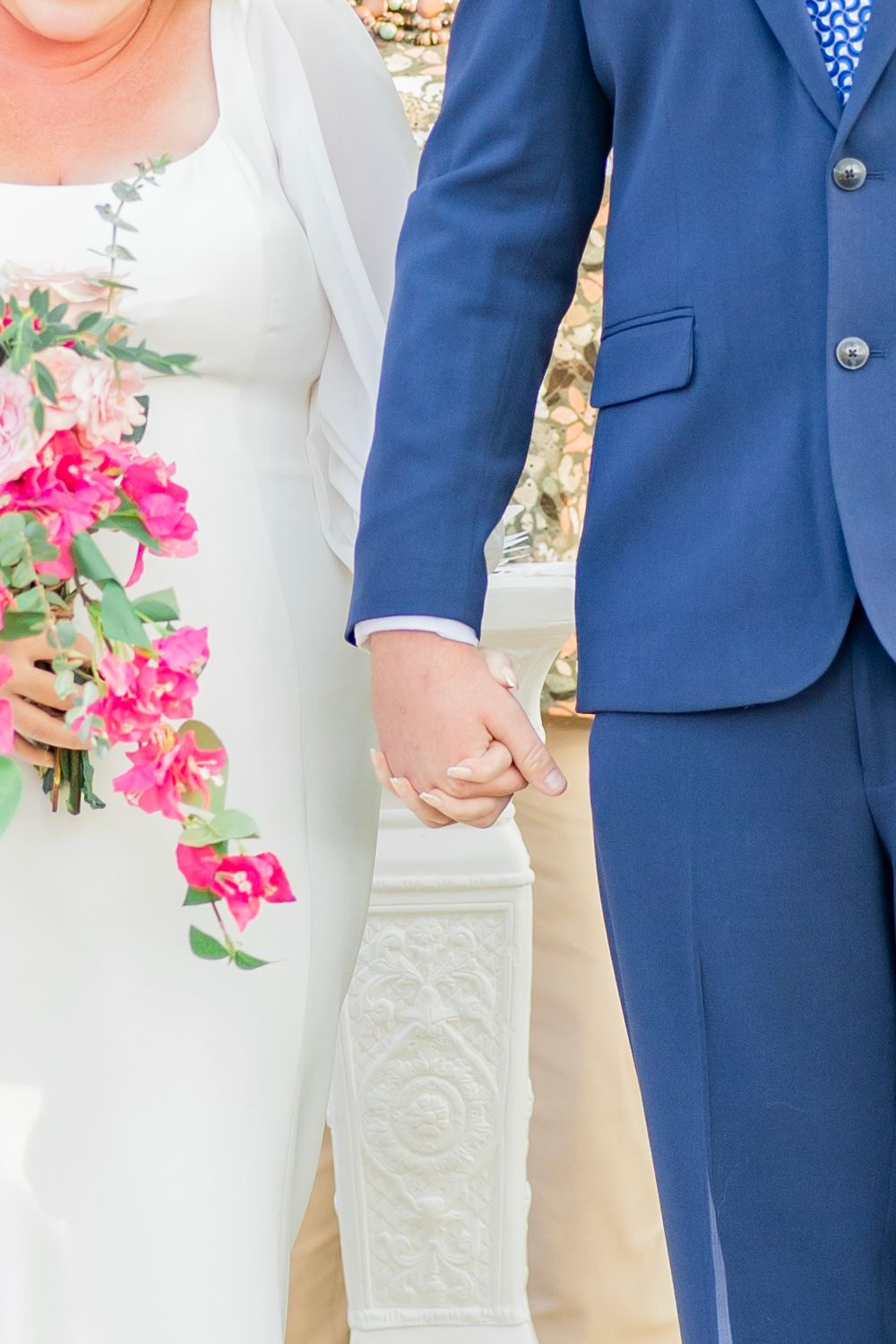 Newlyweds hold hands with bride clutching pink floral bouquet after outdoor wedding ceremony.