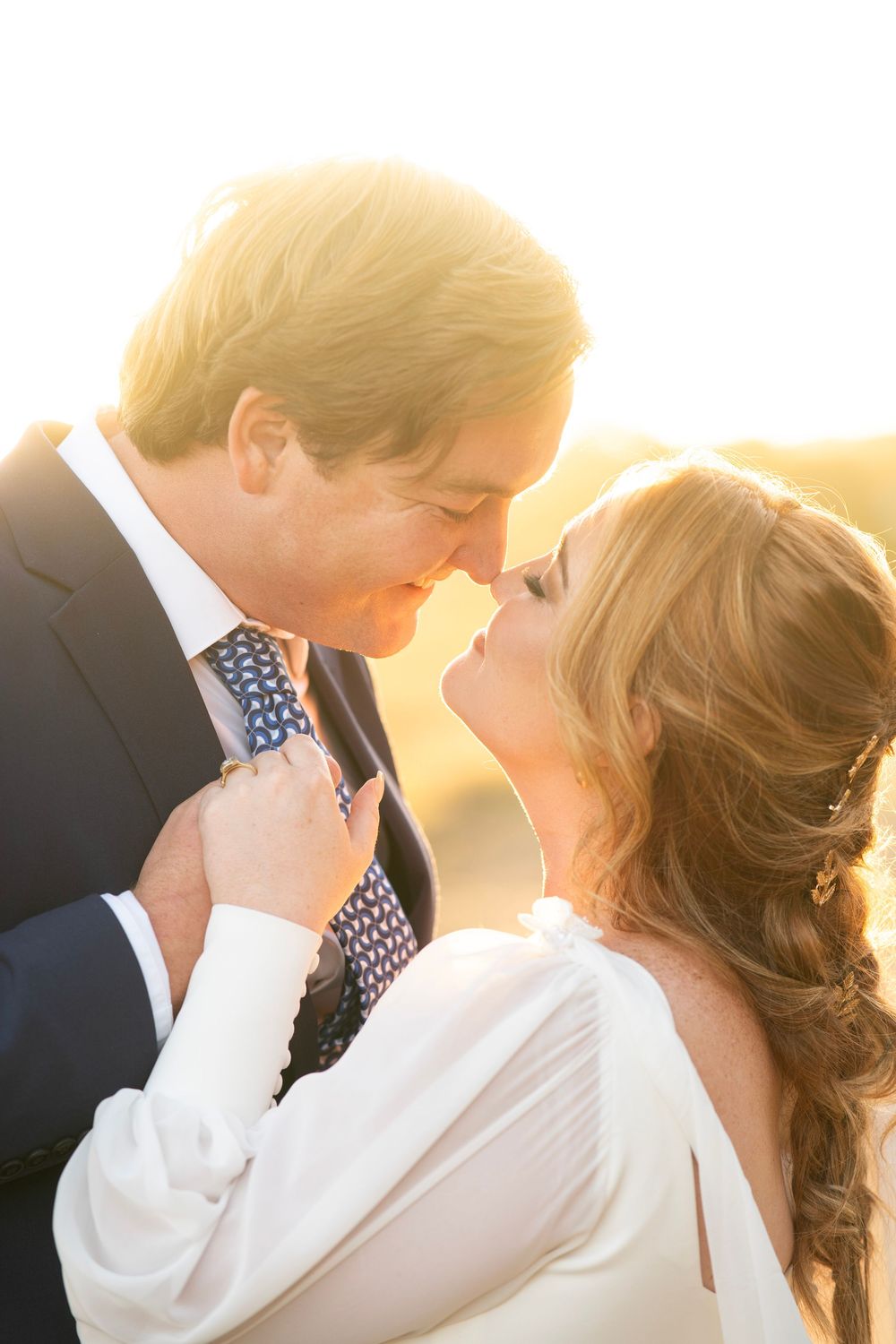 Bride and groom sharing an intimate moment bathed in warm golden sunset light, bride holding grooms tie.