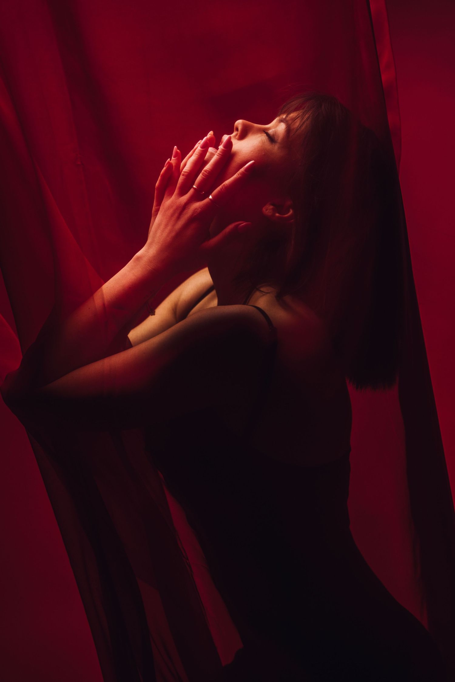 Artistic portrait with hands reaching up in dramatic red lighting and shadows.