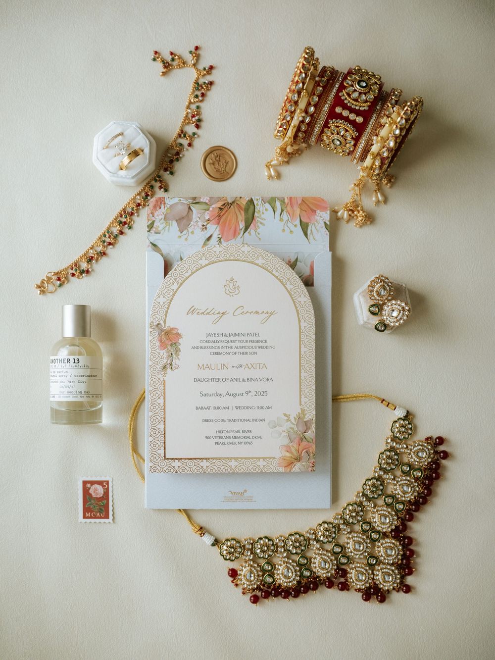 Elegant wedding invitation suite with gold details, floral motifs, and vintage-inspired jewelry laid out on cream surface.