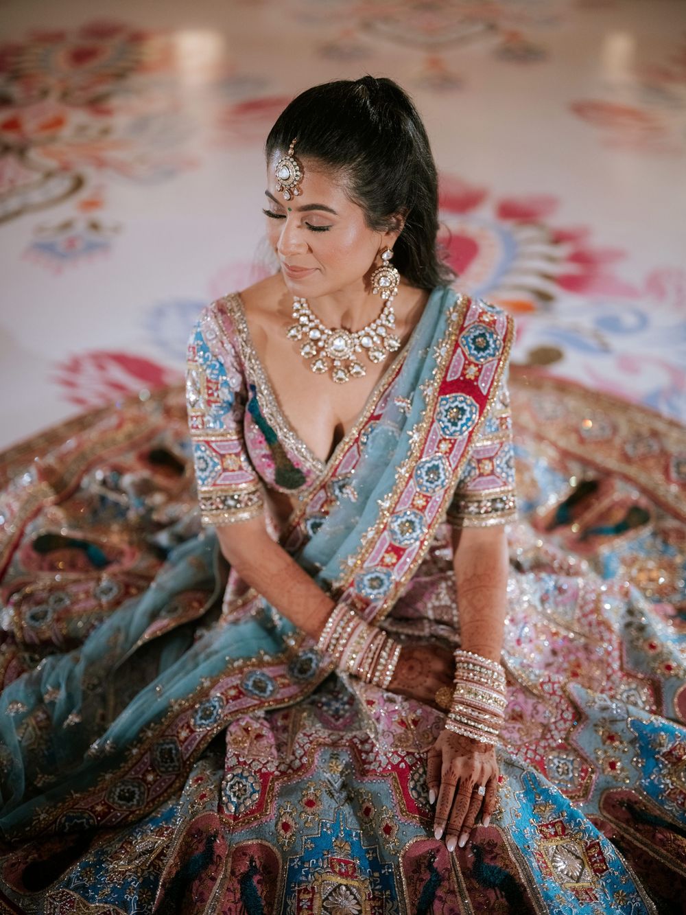 Close-up details of ornate Indian bridal attire featuring intricate embroidery and traditional jewelry in turquoise and pink tones.