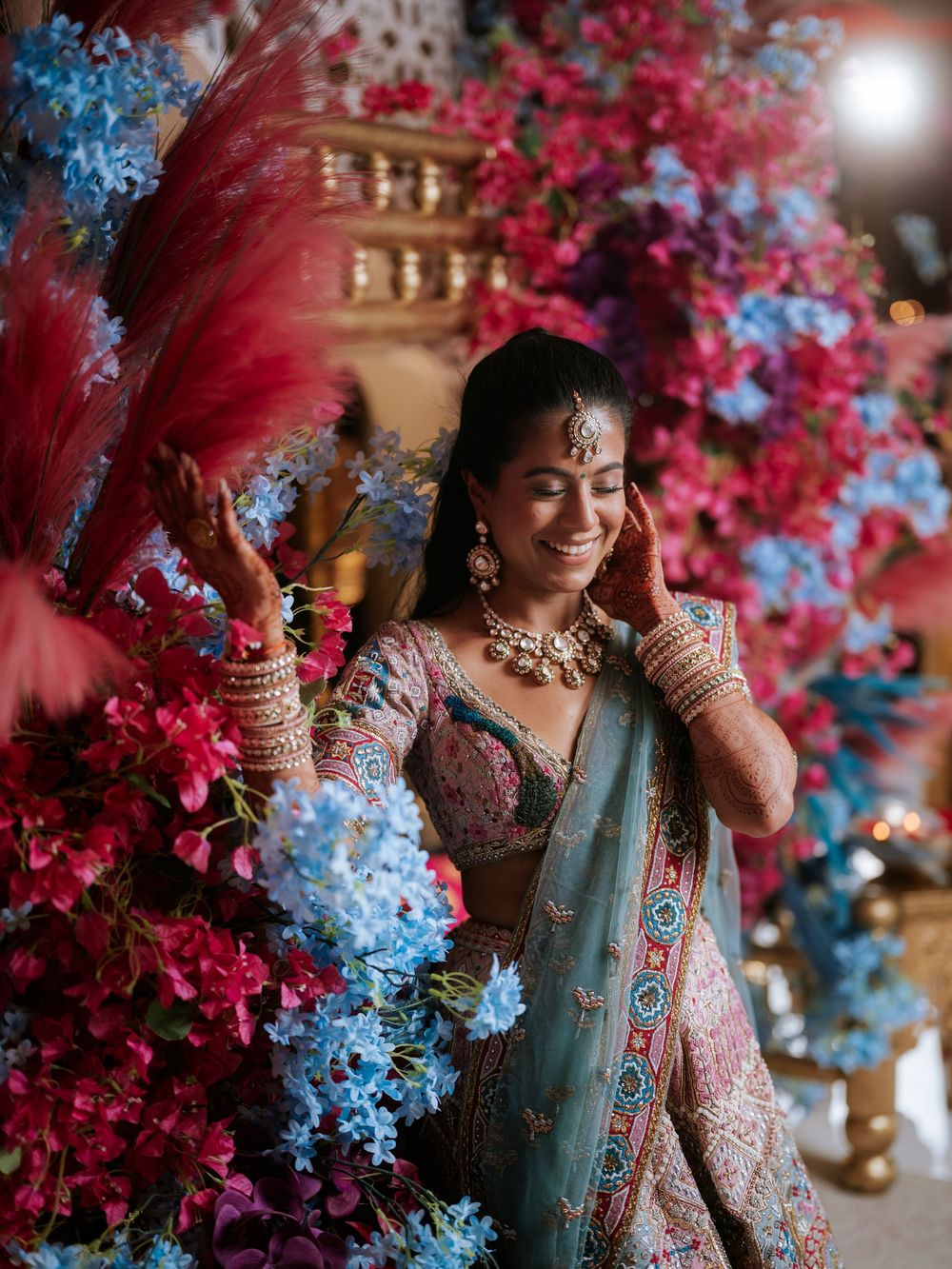 Traditional Indian bridal attire with turquoise lehenga surrounded by vibrant pink and blue floral decorations.