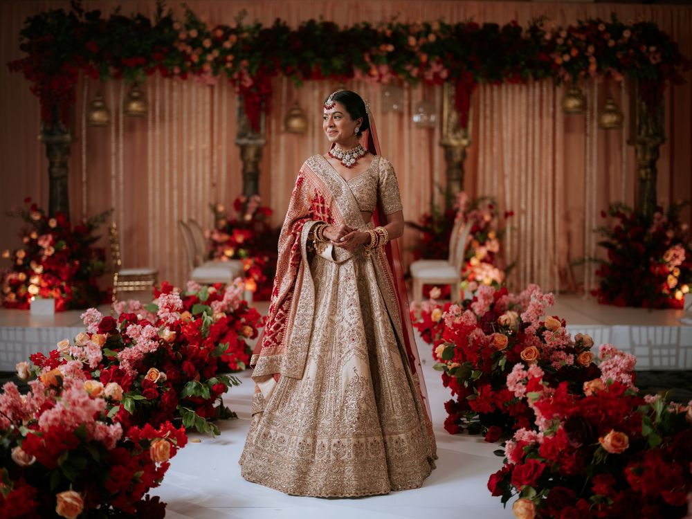 Ornate gold lehenga with intricate embroidery details surrounded by vibrant red floral arrangements in an elegant setting.