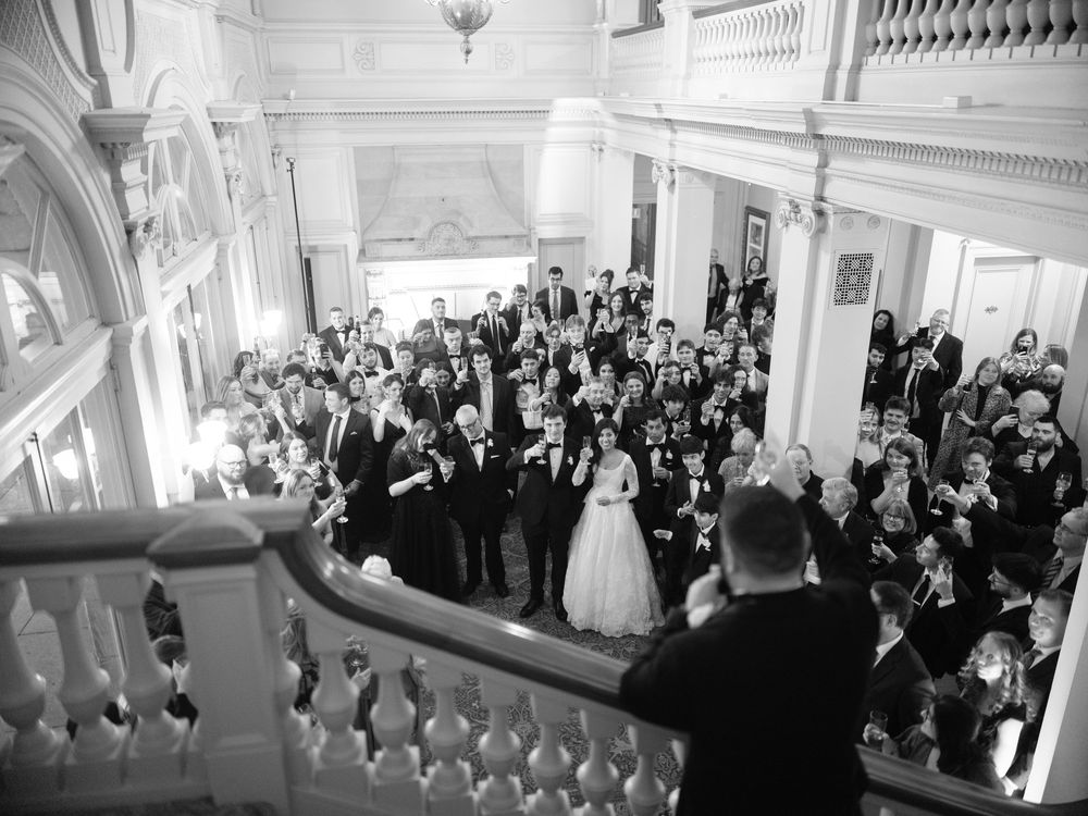 A large crowd of wedding guests stands in an elegant white ballroom during a formal celebration.