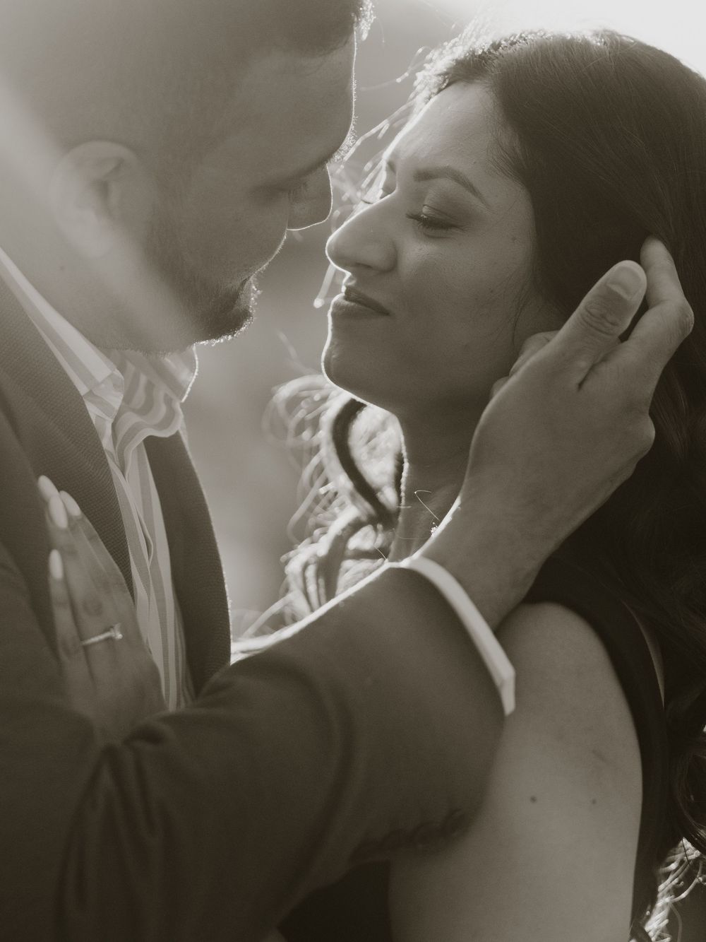 Black and white romantic couple portrait with man tenderly cupping womans face as they lean in for a kiss.