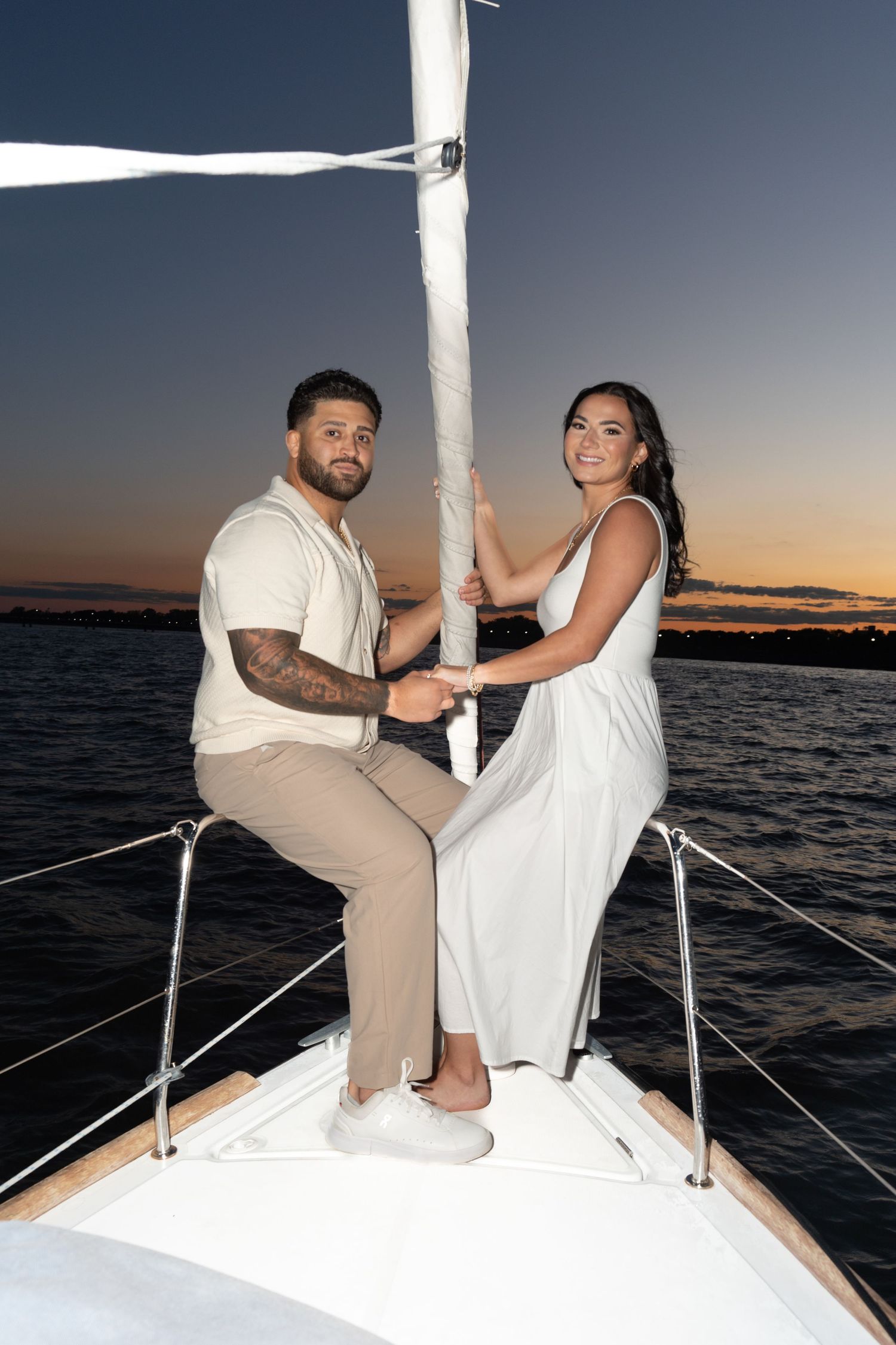 A couple sits together on the bow of a boat at sunset, enjoying a romantic moment on the water.