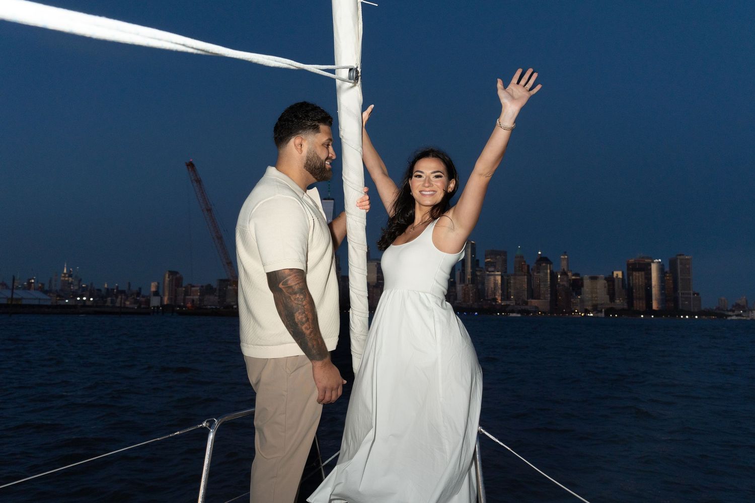 A couple celebrates on a boat at sunset with the New York City skyline visible in the background.