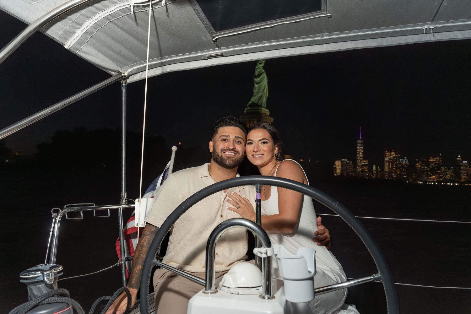 People enjoying a romantic evening boat ride on a yacht with city lights visible in the background.