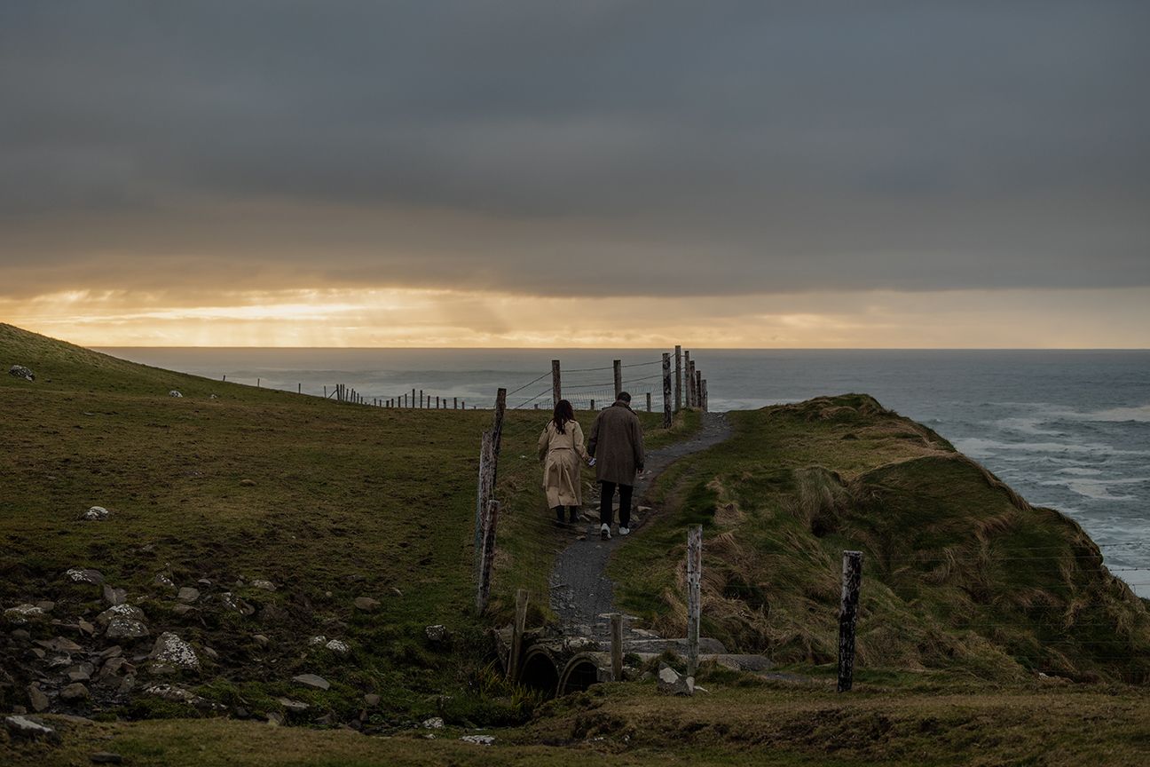 Golden hour engagement portraits with stormy clouds and Atlantic waves at Cliffs of Moher