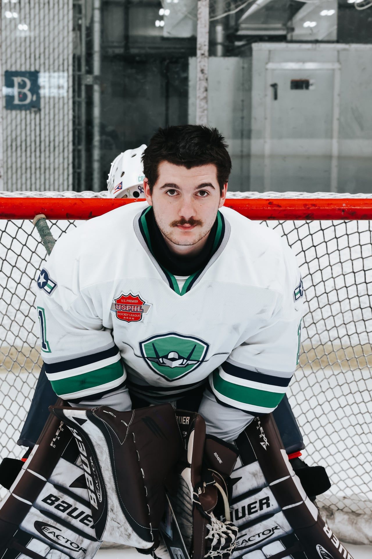 Hockey goalie in white and green jersey positioned in front of the net.