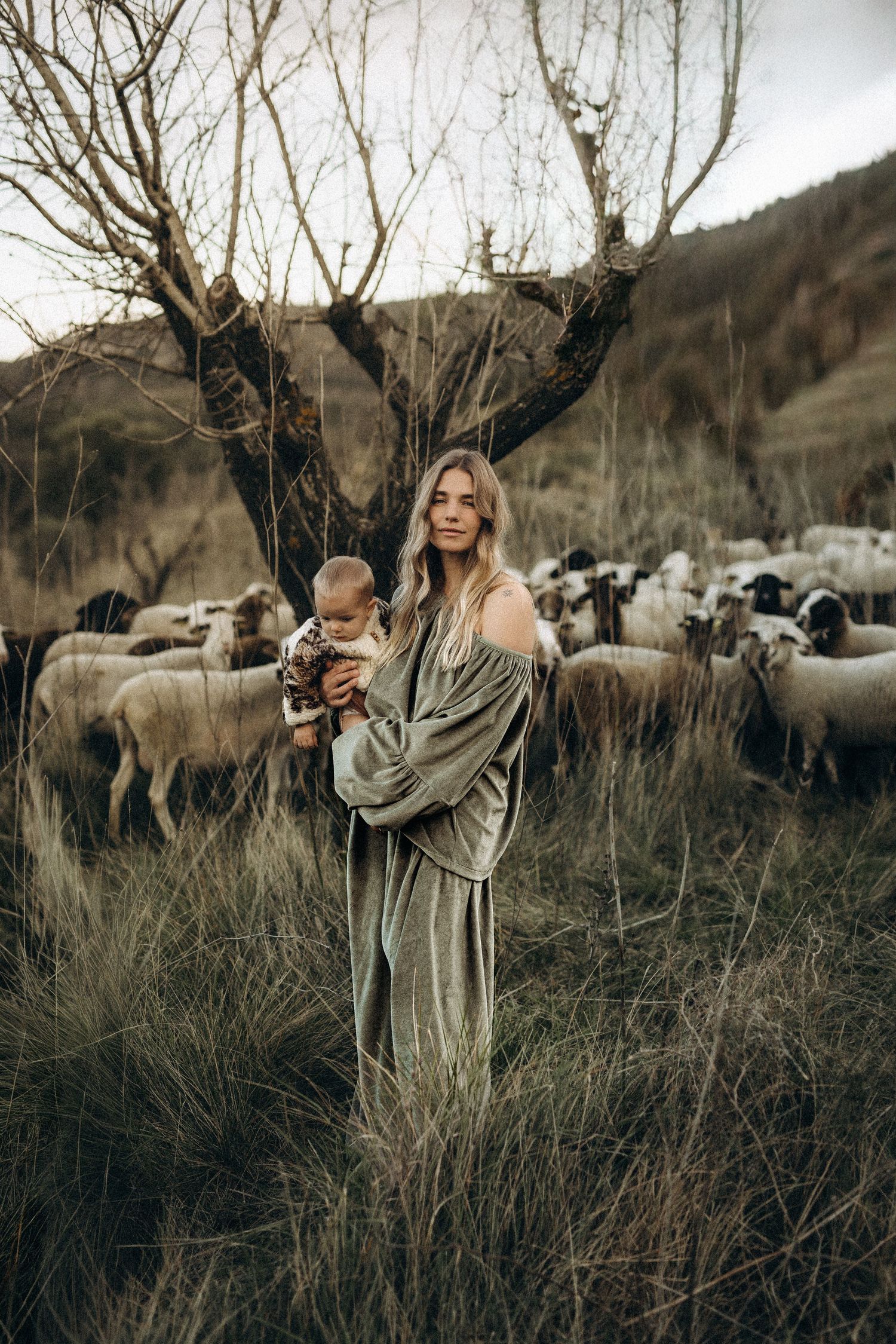 Mother and baby in a in artistic shots in a field with sheep grazing in the background. Javea photographer