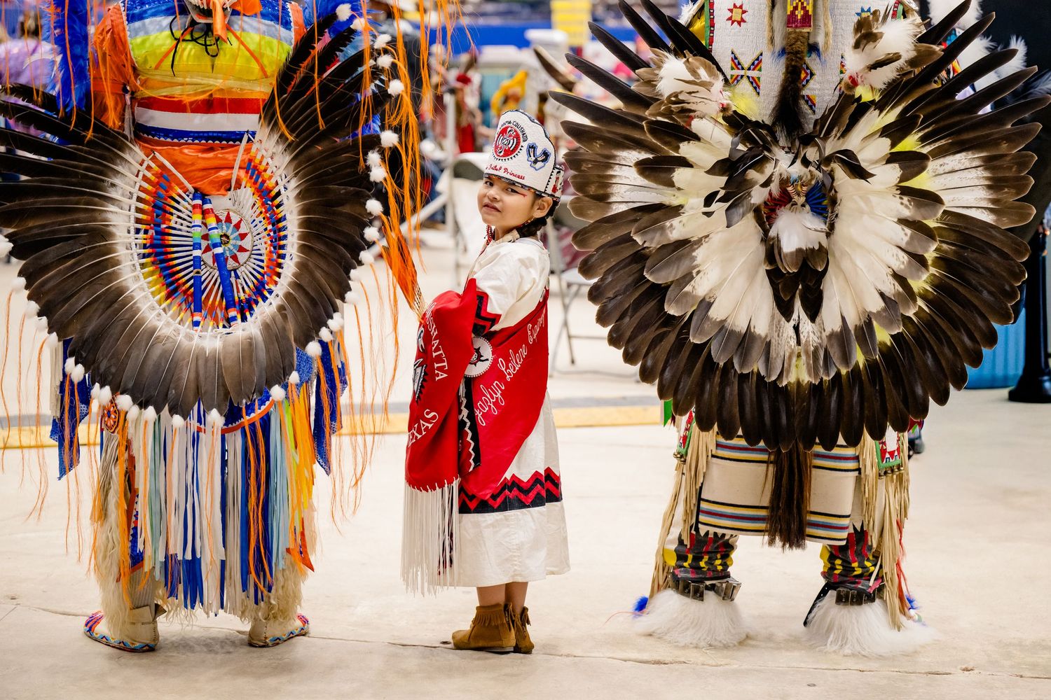 Traditional Native American dancers in colorful ceremonial regalia with feathered headdresses perform at a powwow gathering.