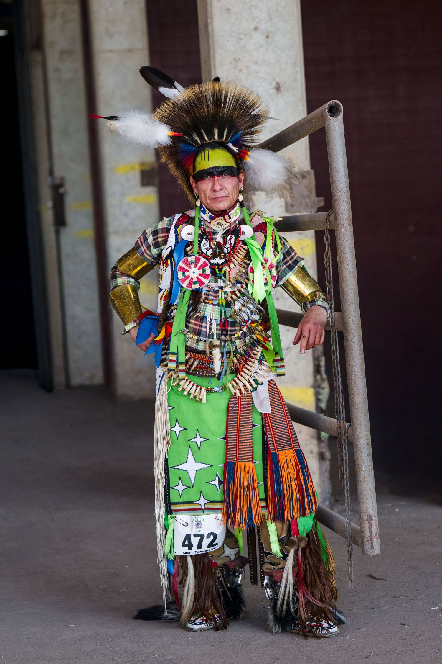 Traditional Native American dancer in vibrant green regalia with feathers and beadwork performs at an indoor venue.