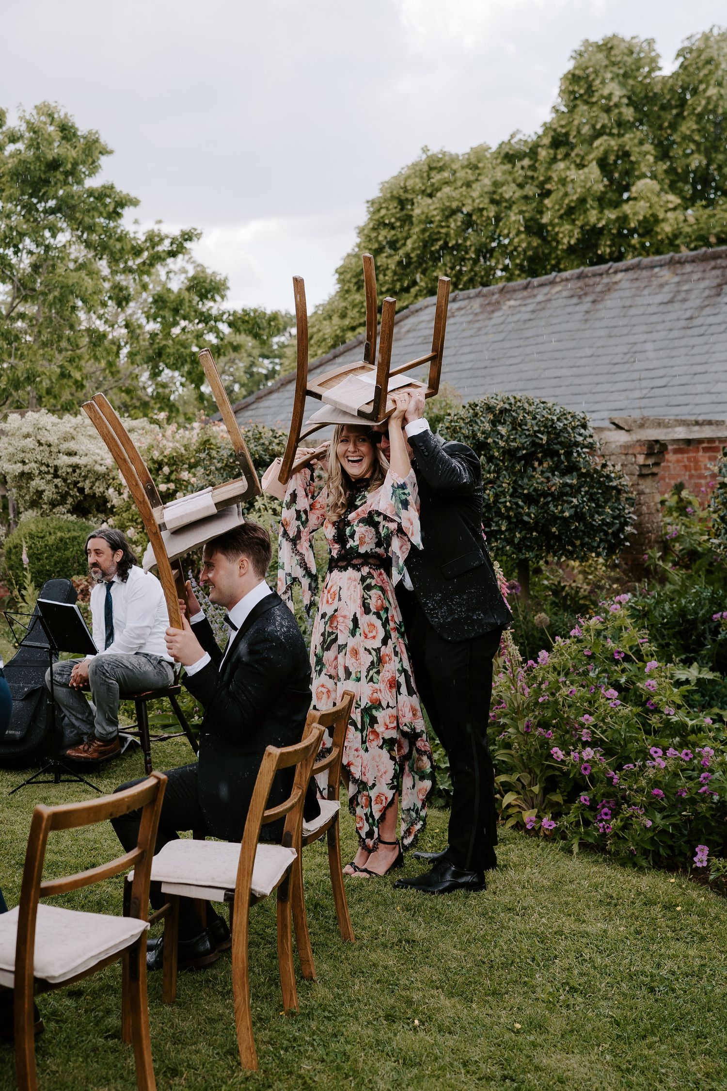 wedding guests taking shelter underneath chairs during a rain shower during wedding ceremony at dewsall court in herefordshire