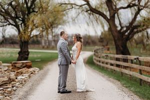 Bride and groom hold hands facing each other on a scenic gravel path lined with trees at their wedding.