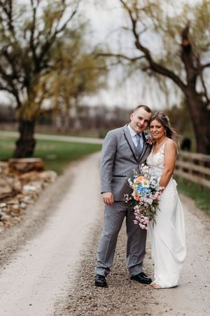 Bride and groom pose together on a rustic gravel path, bride holding a colorful wildflower bouquet at spring wedding.