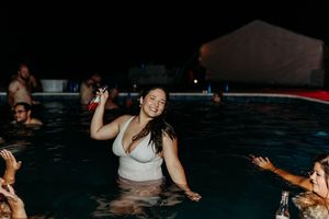 Woman smiling and dancing in a pool at a nighttime outdoor party with other guests around her.