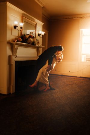 Couple sharing a dramatic dip dance pose in a warmly lit vintage room with a classic fireplace.