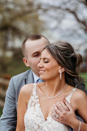 Groom in gray suit tenderly kisses brides cheek as she smiles softly during outdoor wedding portraits.