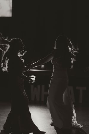 Dramatic black and white silhouette of bride and bridesmaid dancing together at wedding reception.