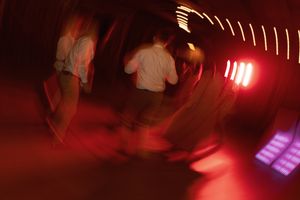 Guests dancing under vibrant red lights creating a blurred motion effect at a lively wedding reception.