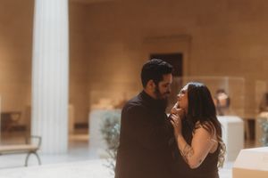 Couple sharing a romantic moment in a warmly lit museum gallery with tall columns.