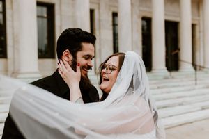Joyful bride and groom sharing intimate moment with veil flowing at courthouse.