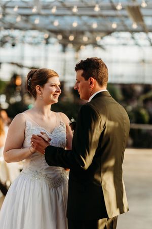 Bride and groom share their first dance under string lights in an elegant greenhouse wedding venue.