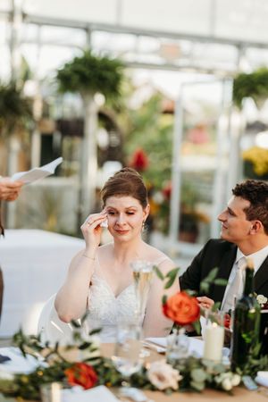 Emotional bride wipes tears during wedding reception speeches at a beautifully decorated table.