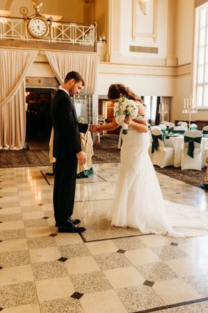 Bride and groom holding hands during first dance in an elegant ballroom venue.