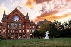 Bride and groom embracing at sunset in front of a stunning red brick historic wedding venue building.