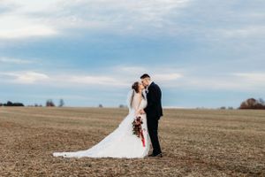 Bride and groom sharing a romantic kiss in an open field under a wide blue sky.