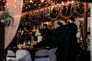 Wedding ceremony under warm string lights with bride, groom, officiant and wedding party at decorated altar.