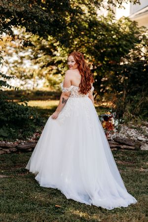 Redhead bride in off-shoulder ballgown holds bouquet in garden setting.