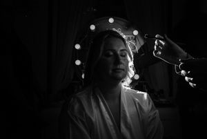 Dramatic black and white image of bride having veil placed with glowing vanity lights surrounding her.