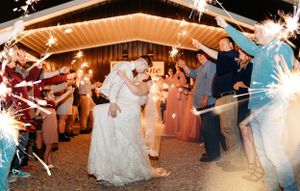 Bride and groom kissing during a sparkler exit surrounded by cheering wedding guests at night.