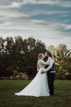 Bride and groom sharing a kiss on a lush green lawn with trees in the background.