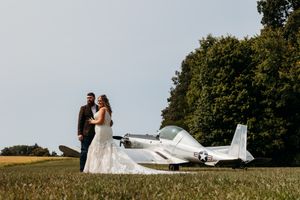 Wedding couple posing together in a field beside a classic white military airplane on a sunny day.