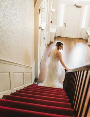 Bride in white gown and veil ascends red-carpeted staircase in elegant venue.
