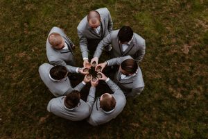 Aerial view of groomsmen in gray suits forming a circle with drinks.