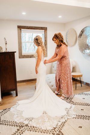 Mother helps bride in elegant lace wedding gown with long train.