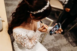 Bride in lace wedding dress and floral crown writing on phone during wedding ceremony.