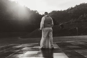 Black and white photo of bride and groom embracing on dance floor with sunlit hillside backdrop.