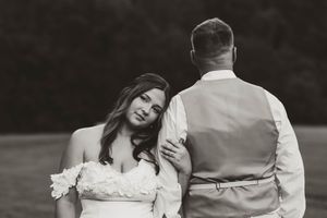Black and white photo of bride in off-shoulder gown leaning on grooms back in an open field.