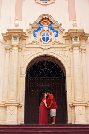 Couple sharing romantic kiss at ornate church entrance with baroque architecture.