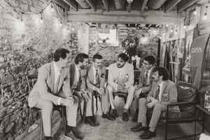 Groom and groomsmen relaxing and chatting in rustic stone venue with string lights in black and white photo.